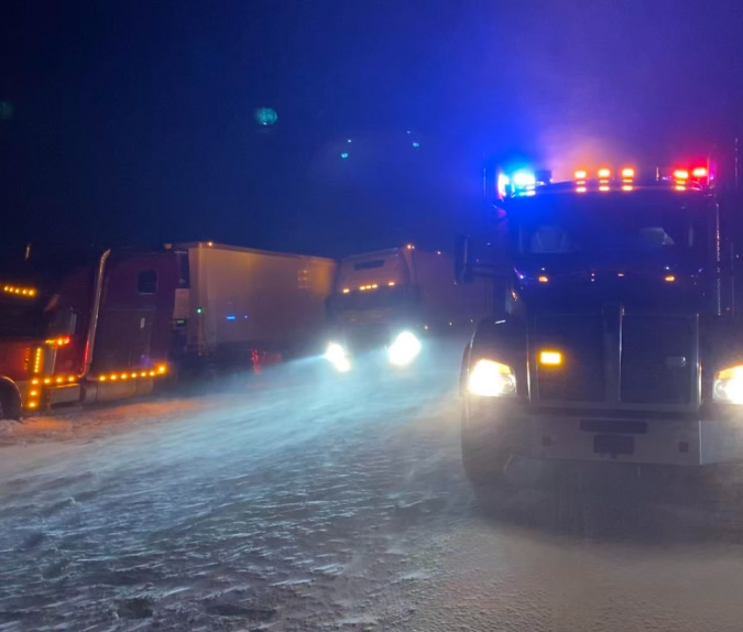 Heavy-duty tow truck performing winter accident recovery on a snowy Wyoming highway, transporting a damaged semi-truck during emergency roadside assistance near Cheyenne and Laramie.