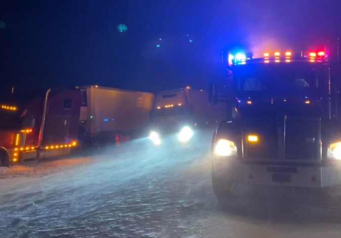 Heavy-duty tow truck performing winter accident recovery on a snowy Wyoming highway, transporting a damaged semi-truck during emergency roadside assistance near Cheyenne and Laramie.
